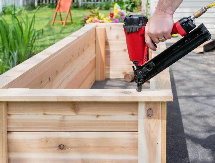 Ein Mann baut ein Hochbeet aus Holz zusammen.