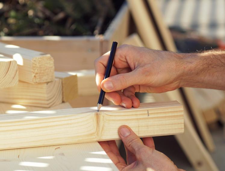 Nahaufnahme einer Hand, die Holz mit Bleistift markiert.