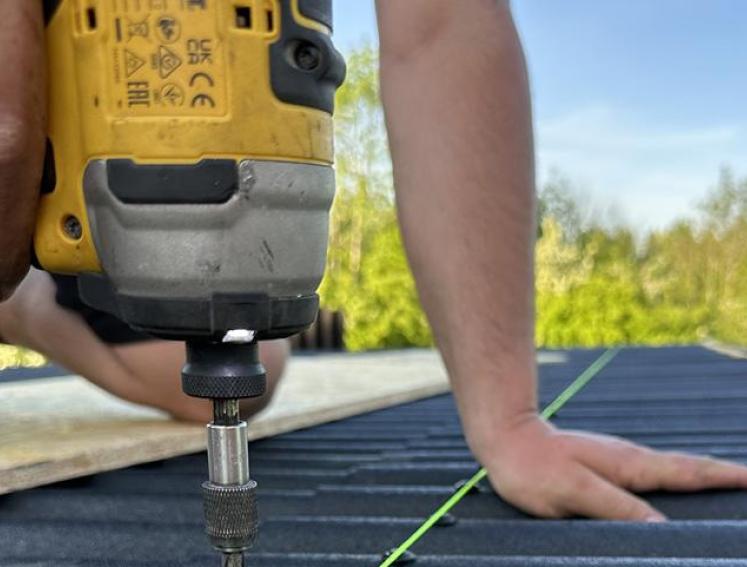 Ein Handwerker verschraubt beim Overroofing Bitumenwellplatten auf einem Gartenhaus.