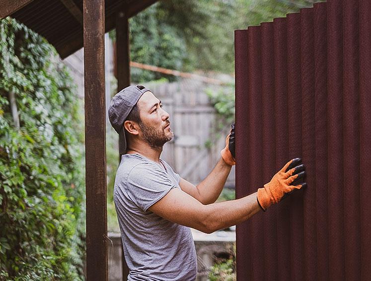 Ein Handwerker hält eine ONDULINE BASE Bitumenwellplatte in den Händen.