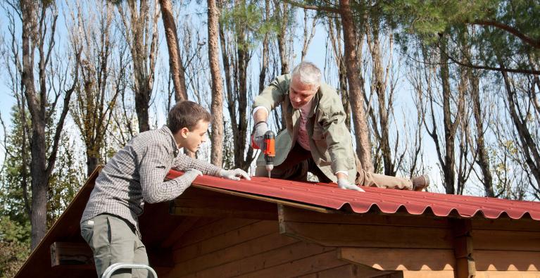 Ein Vater und sein Sohn decken ein Gartenhaus mit Bitumenwellplatten.